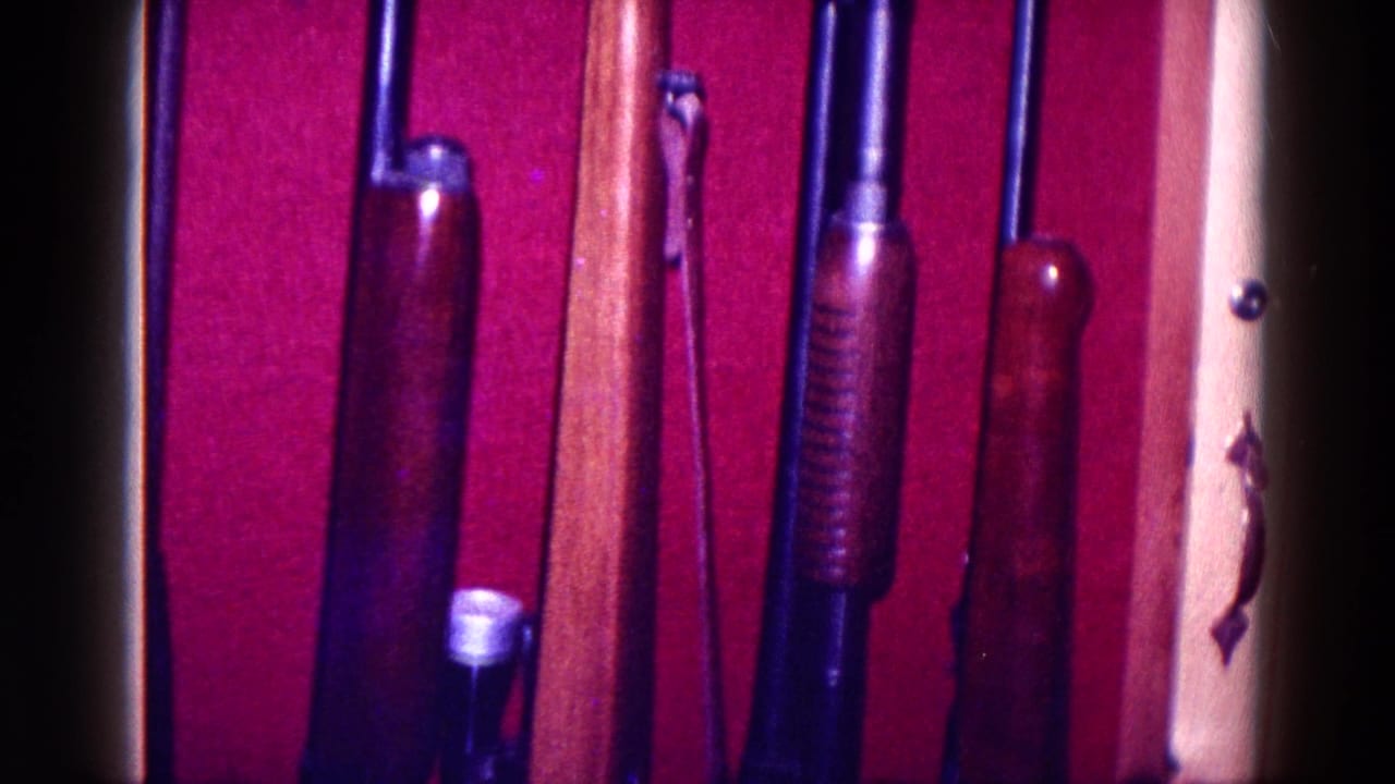 1968 Minnesota home-movie frame with rifles or shotguns standing against deep red lining inside a wooden display cabinet.
