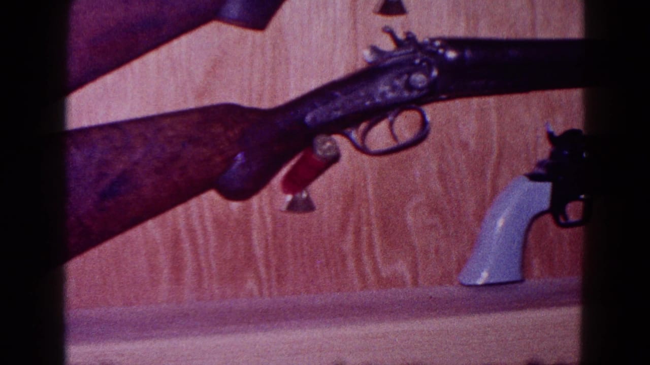 1968 Minnesota home-movie frame with a mounted long gun above a partially visible light-handled revolver.