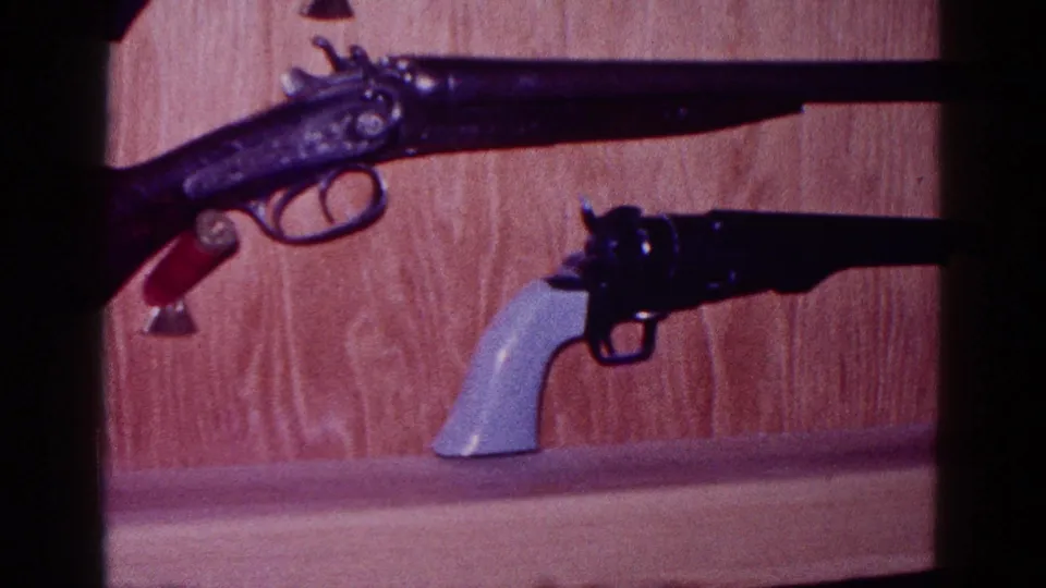1968 Minnesota 8mm frame showing a mounted long gun over a revolver with a pale grip on a shelf.