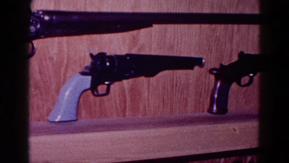 1968 Minnesota frame showing two revolvers displayed on a shelf below a mounted long gun barrel.