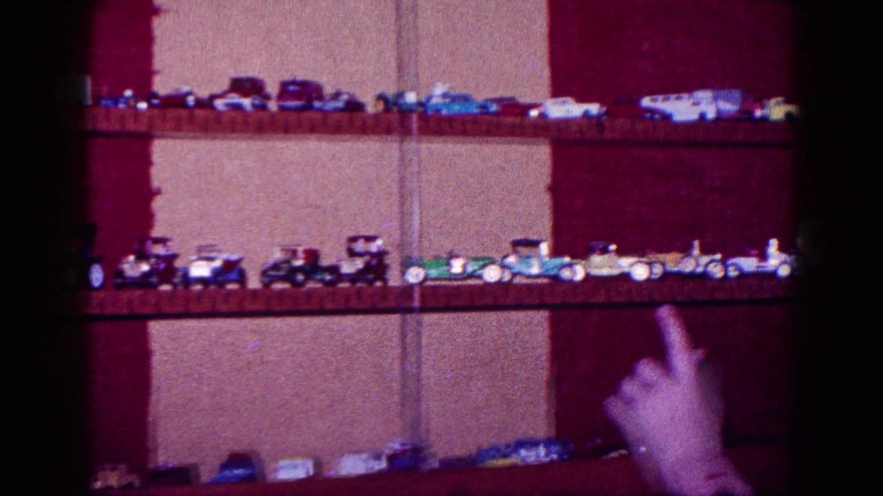 1968 Minnesota 8mm frame showing a hand pointing toward rows of toy cars and trucks on wooden shelves.
