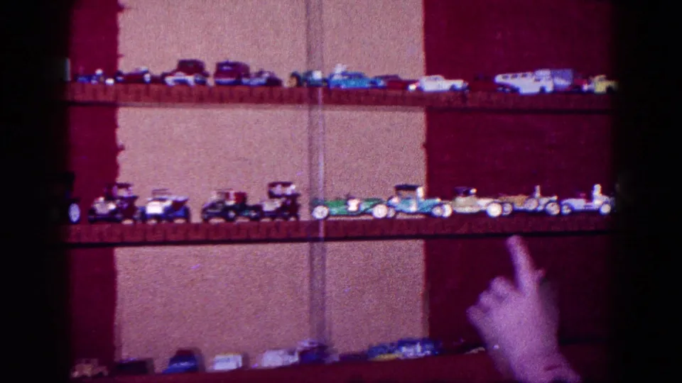 1968 Minnesota 8mm frame showing a hand pointing toward rows of toy cars and trucks on wooden shelves.