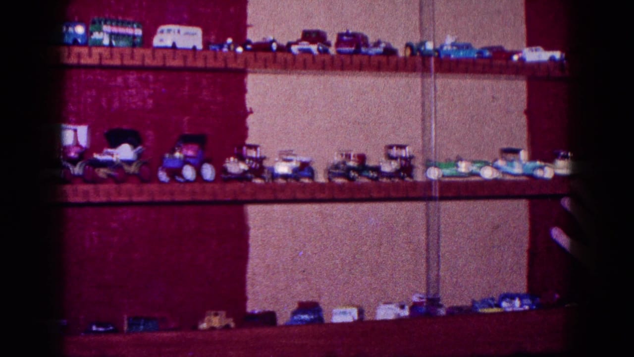 1968 Minnesota home-movie frame with miniature cars and trucks displayed across wooden shelves against red and beige walls.