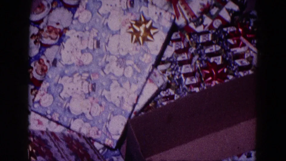 1968 Minnesota 8mm frame showing close-up holiday wrapping, foil bows, and a partially open box in a private interior.