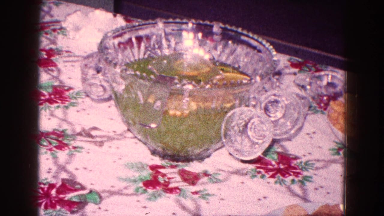 Glass punch bowl with green punch on a floral holiday tablecloth.