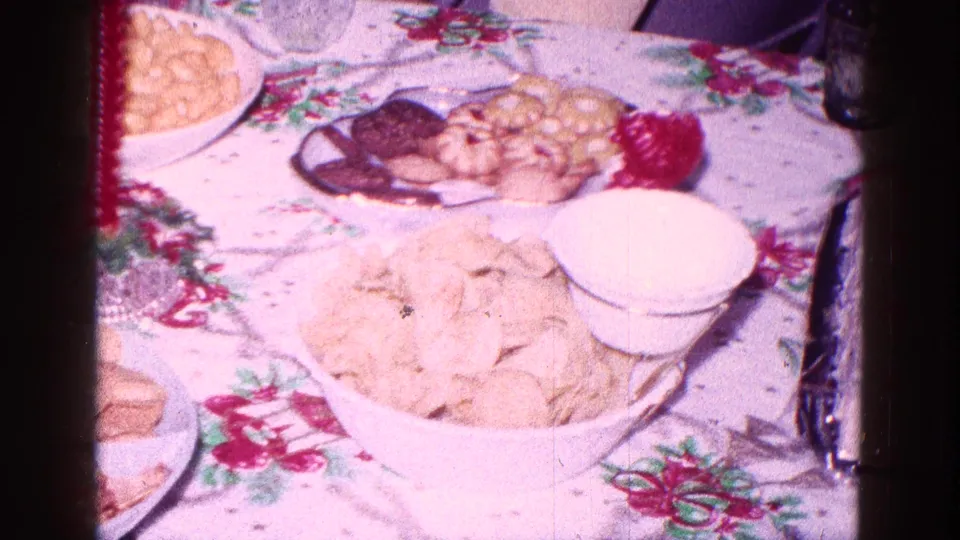 1968 Minnesota home-movie view of a holiday snack spread with chips, crackers, cookies, a white bowl, and red candle.