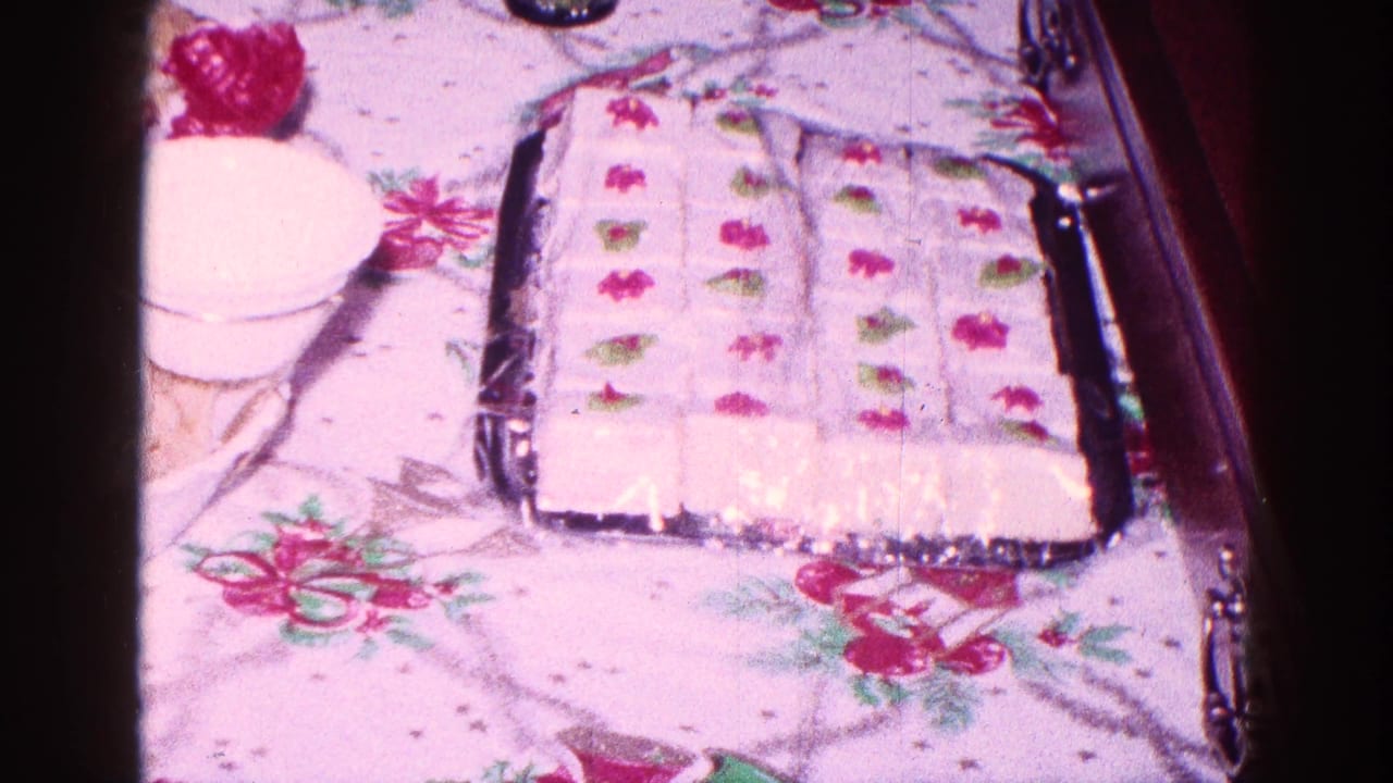 Decorated rectangular cake on a floral tablecloth beside a dessert cup.