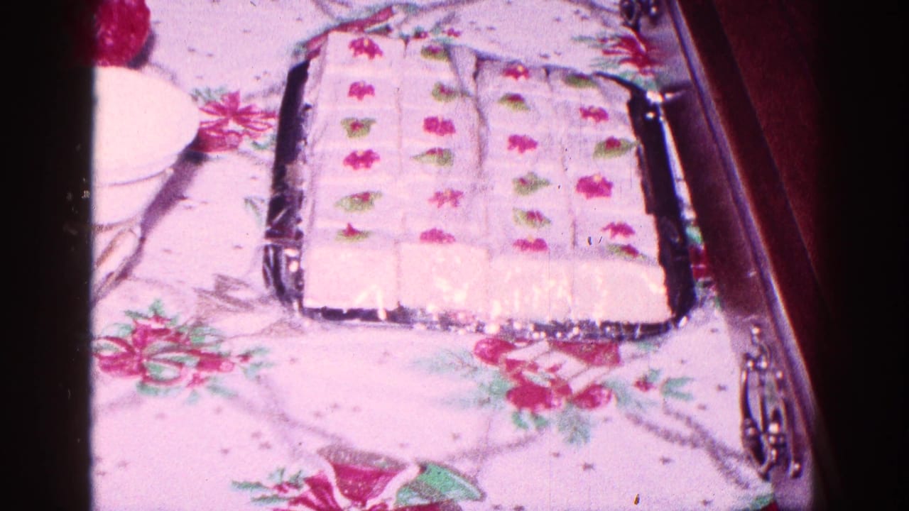 Rectangular decorated cake on a tray with floral tablecloth around it.