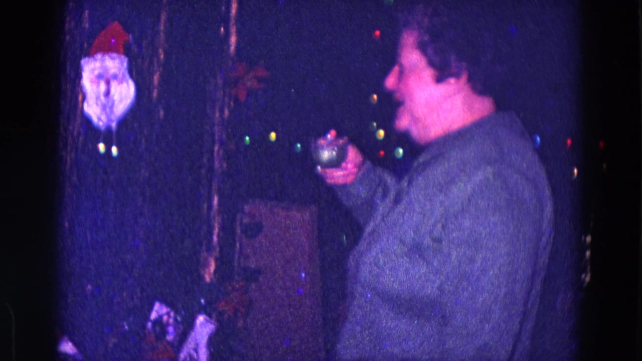 Woman in a gray sweater holds a small glass near Christmas lights and a Santa decoration.