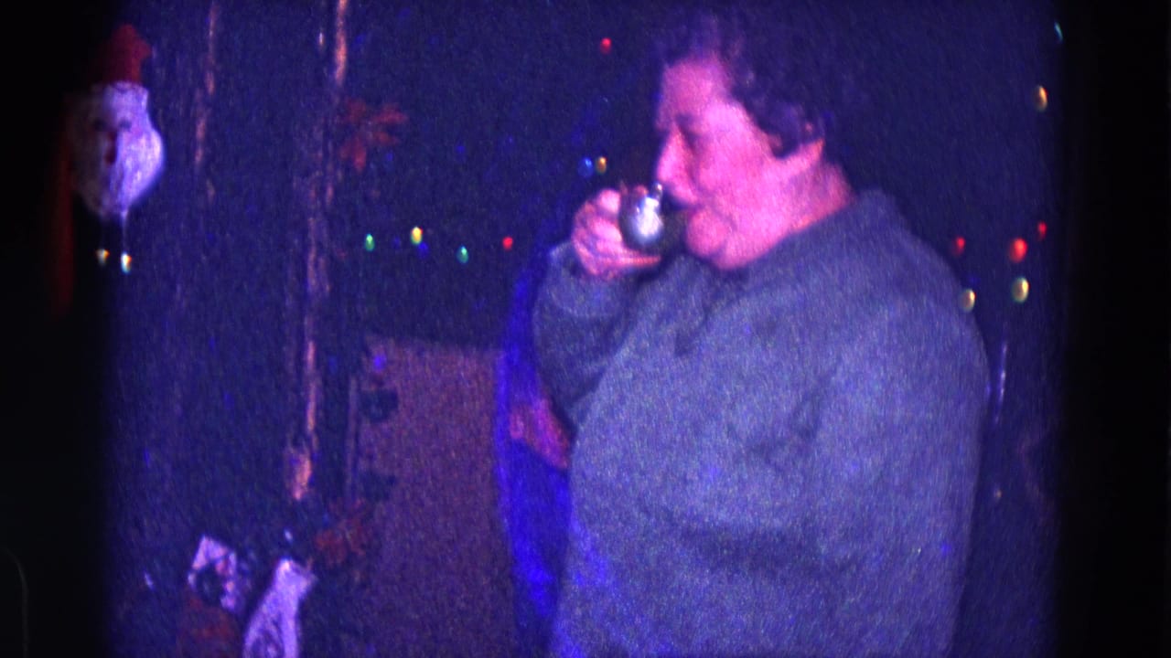 Woman raises a small glass to her mouth beside colored Christmas lights.
