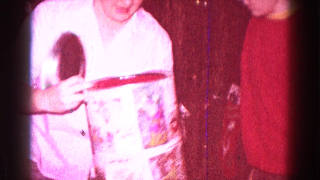 Two people near a cylindrical gift box, with one person in a light shirt holding the box.