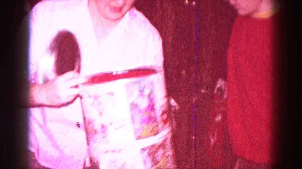 1968 Minnesota home-movie frame showing people close to the camera as a cylindrical gift box is opened indoors.
