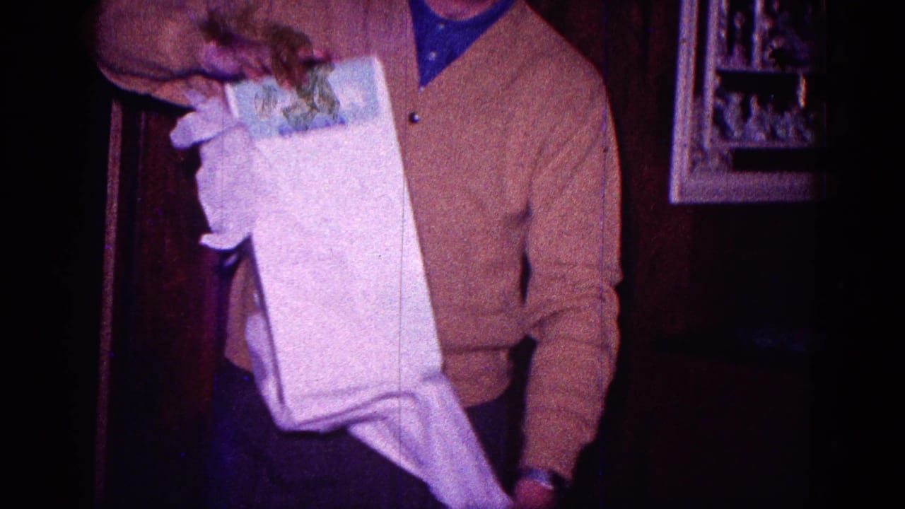 The man lifts paper away from a tall white box in the dim home interior, with product labeling partly visible on the package.