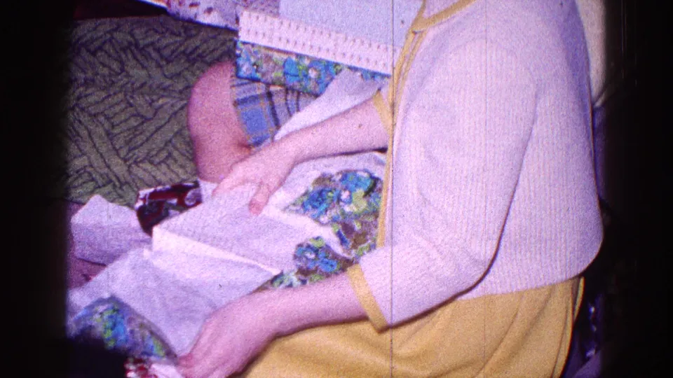 A close home-movie view shows the child uncovering white box or tissue material under the floral gift wrap.