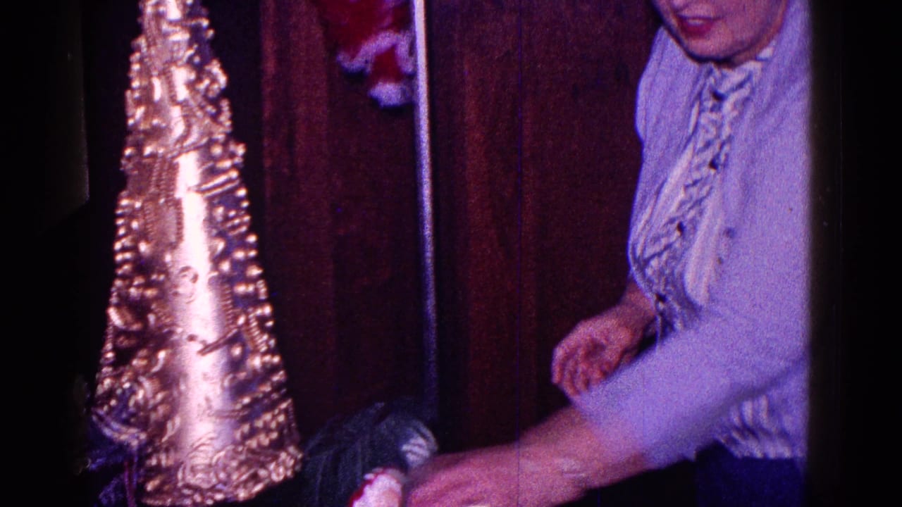 1968 Minnesota home-movie frame showing a woman near a tall metallic cone Christmas decoration in a private interior.
