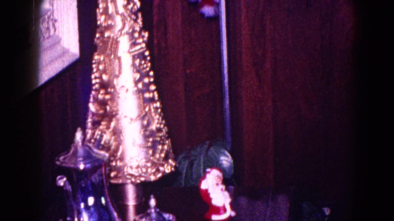 Close 1968 Minnesota home-movie view of a gold cone decoration, small Santa figurine, and silver-toned serving piece indoors.