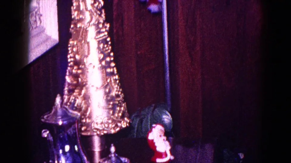 Close 1968 Minnesota home-movie view of a gold cone decoration, small Santa figurine, and silver-toned serving piece indoors.