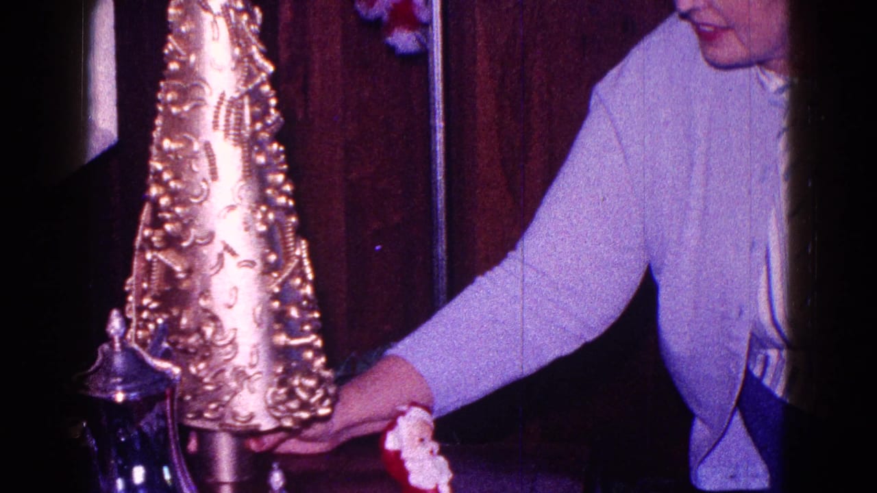 Woman reaches toward a gold Christmas table ornament beside a small Santa figure.