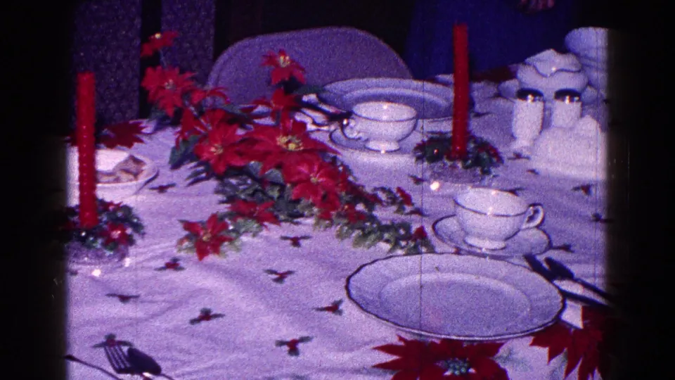 A formal Christmas table setting shows white china, red poinsettias, cups, plates, and a red taper candle in 1968 Minnesota footage.