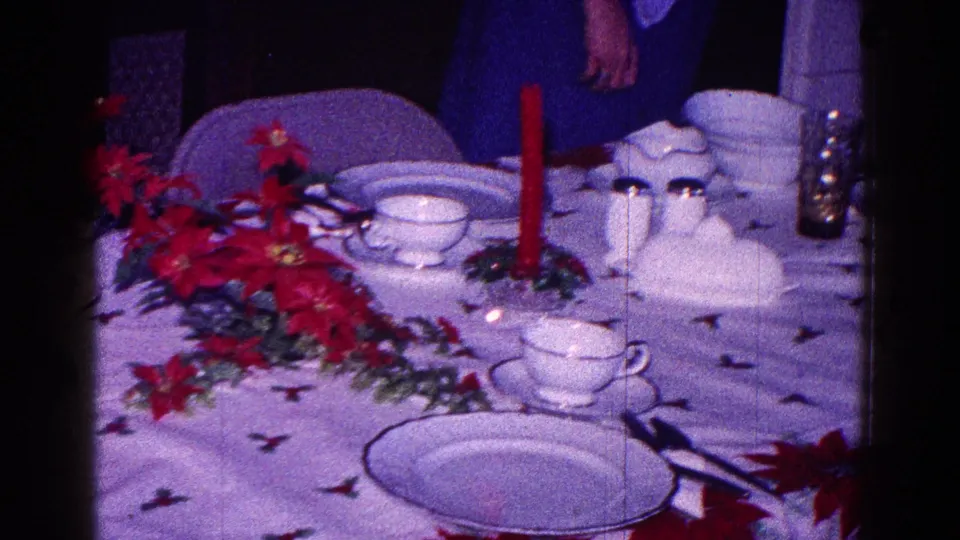 The camera holds on a 1968 Minnesota Christmas table with poinsettias, white dishes, cups, silverware, and a red candle.