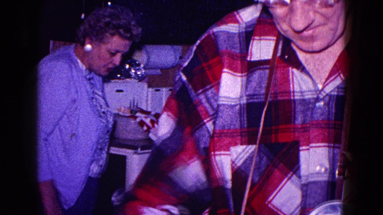 Woman works near the kitchen counter while a man in a red plaid shirt stands in the foreground.