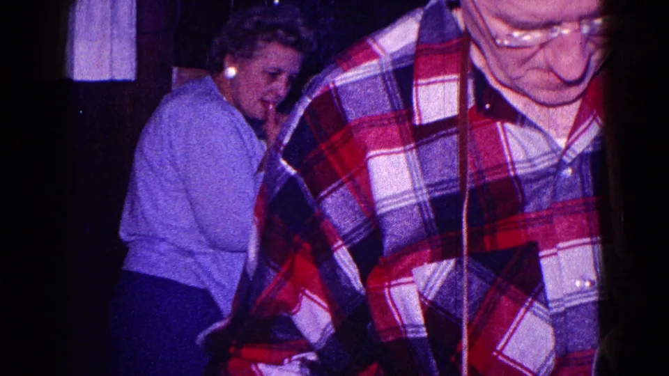 A handheld 1968 Minnesota home-movie view of a woman near the dinner table and a man in plaid partly blocking the frame.