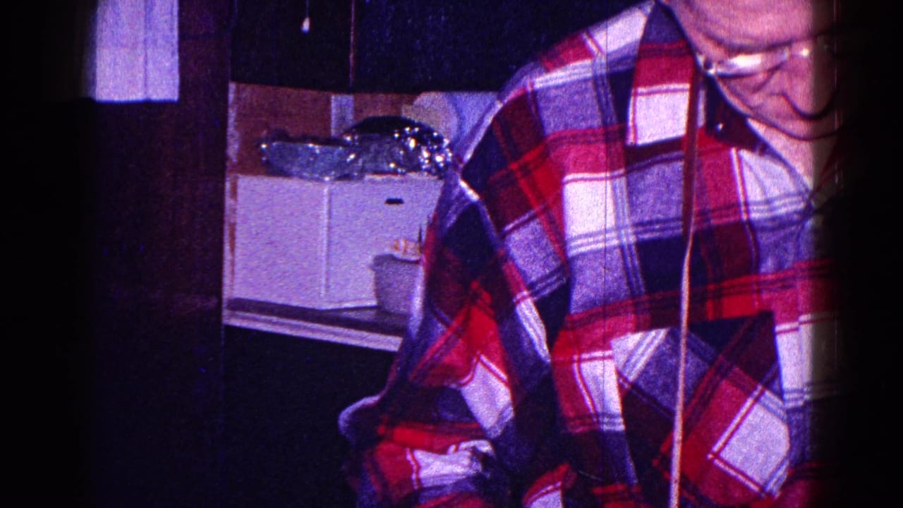 Man in a plaid shirt standing in a kitchen beside a counter and white appliance.