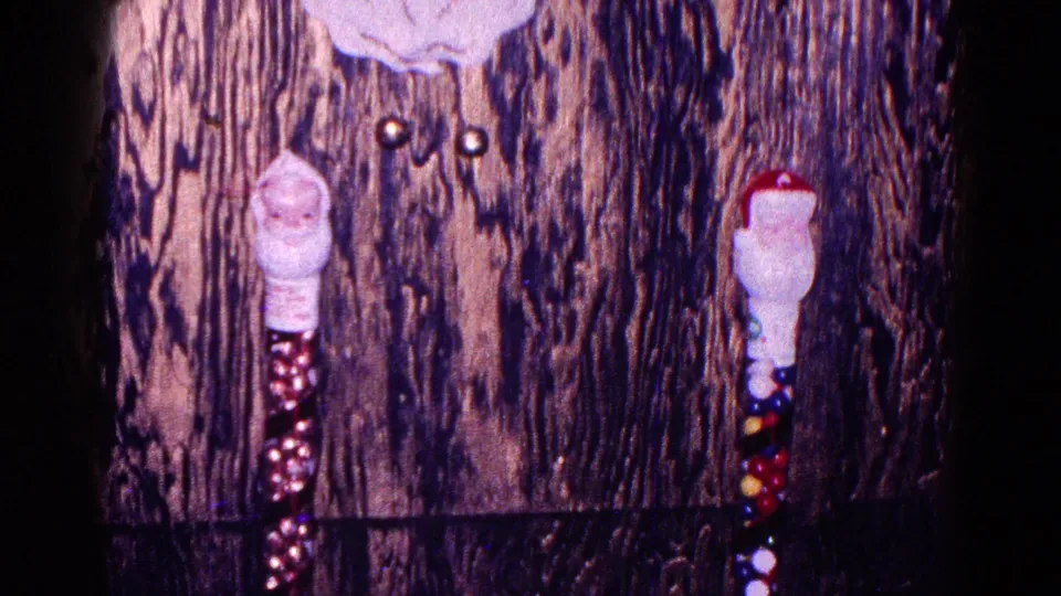 A close 8mm view of Santa-themed decorations hanging on wood paneling in a Minnesota Christmas interior.
