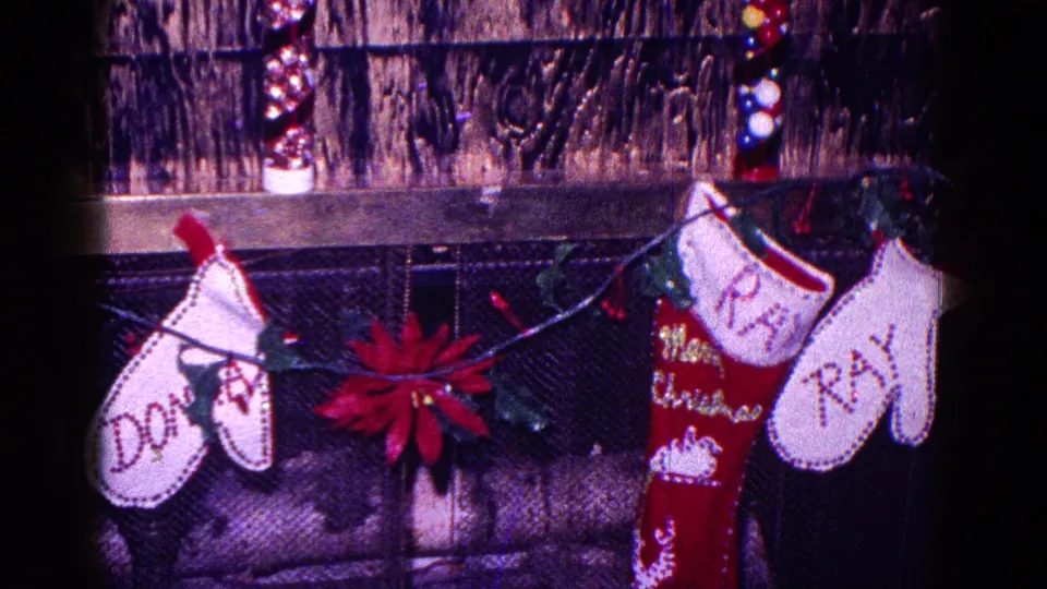 A family Christmas mantle in 1968 Minnesota with named stockings, a red poinsettia, lights, and hanging Santa decorations.