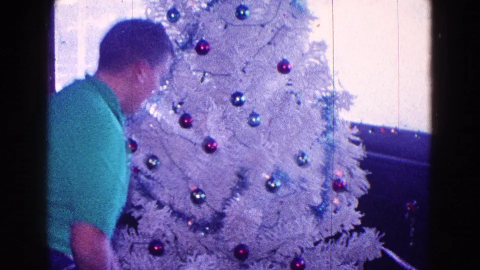 1968 Minnesota home-movie frame with a man near a white Christmas tree decorated with red and blue ornaments.