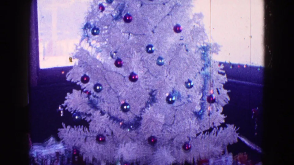 White artificial Christmas tree in a Minnesota 1968 home interior, with colored ornaments and wrapped presents beginning to show below.