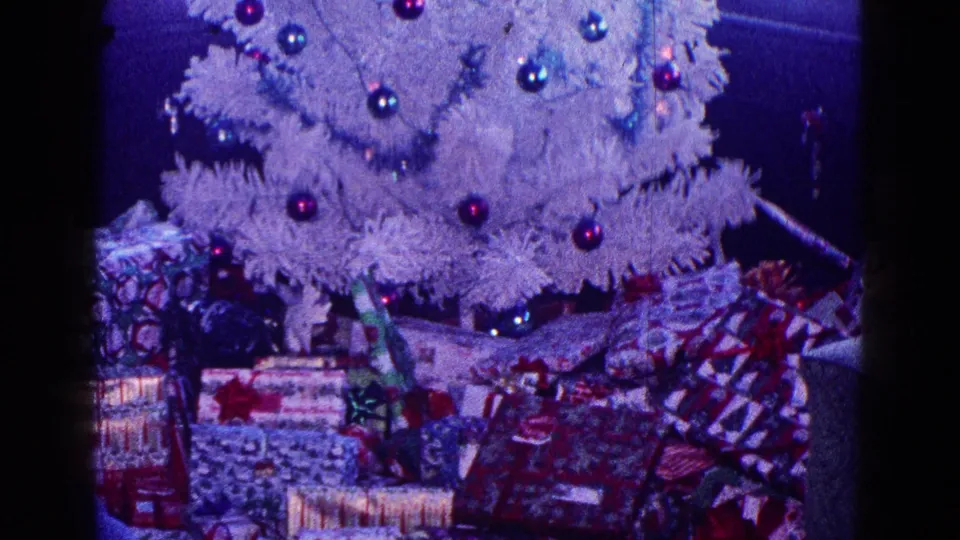 1968 Minnesota home-movie frame showing a white Christmas tree with red and blue ornaments and wrapped presents beneath it.