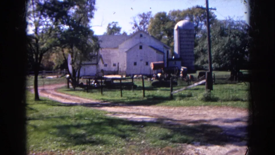 1968 Wauconda, Illinois farm view with a large white barn, tall silo, fencing, dirt driveway, trees, and equipment near the buildings.