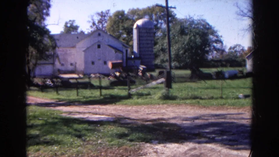 A shifted 1968 Wauconda farm view shows the barn and silo with a tractor or farm equipment near the fence and a dirt driveway in front.