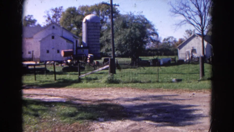 Final 1968 Wauconda frame shows the white barn and silo, a small outbuilding at right, fenced grass, trees, and dirt driveway.