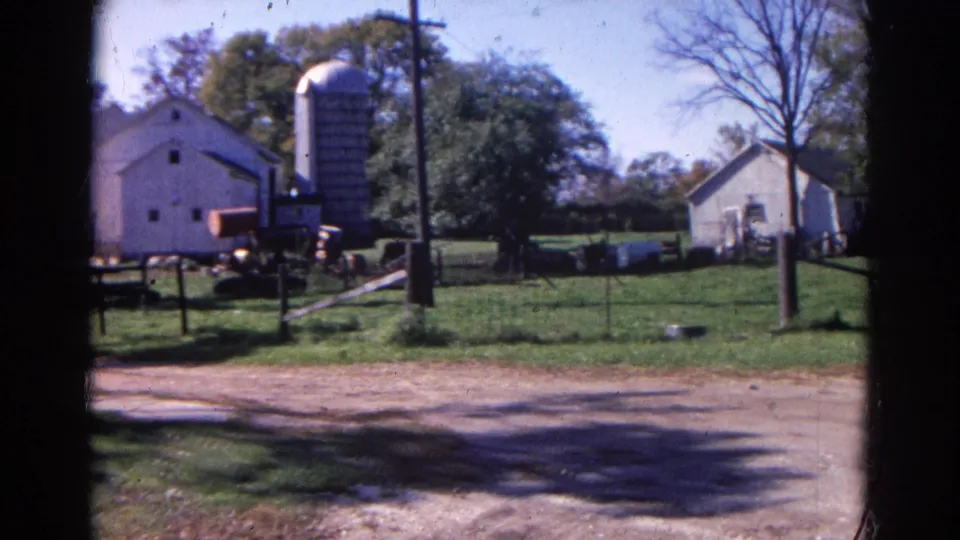 1968 Wauconda, Illinois farm exterior with white buildings, a tall silo, trees, fence posts, grass, and a dirt road.