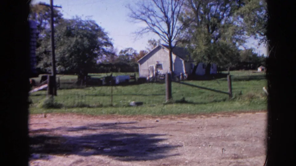 1968 Wauconda farmstead frame with a white building, trees, fence posts, grass, dirt road, and partial silo at the edge.