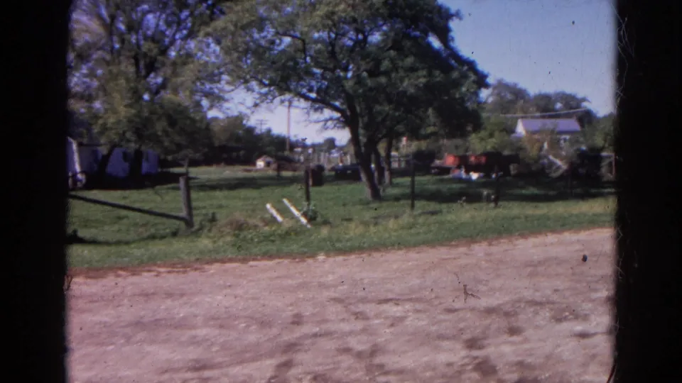 1968 Wauconda, Illinois 8mm frame with a large tree over a grassy yard, fence posts, scattered items, and a house beyond.
