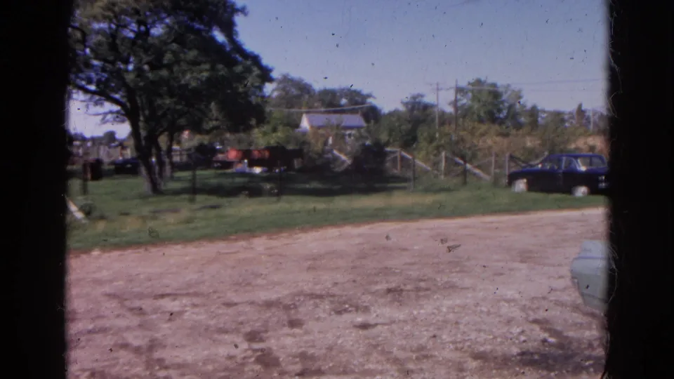 1968 Wauconda, Illinois home-movie frame showing a rural roadside, parked cars, trees, grass, and fields.