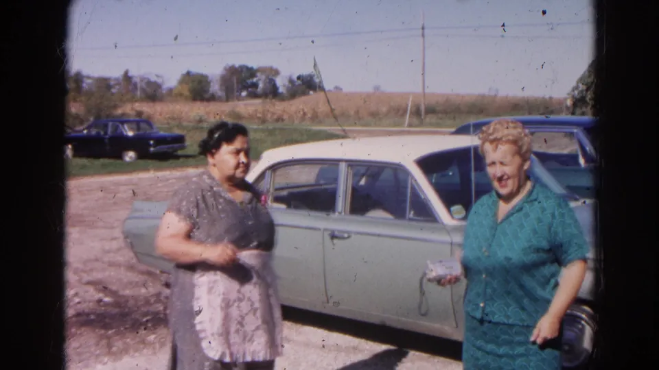 The 1968 Wauconda home movie shows two women beside a classic two-tone sedan, one holding a small object near the car.