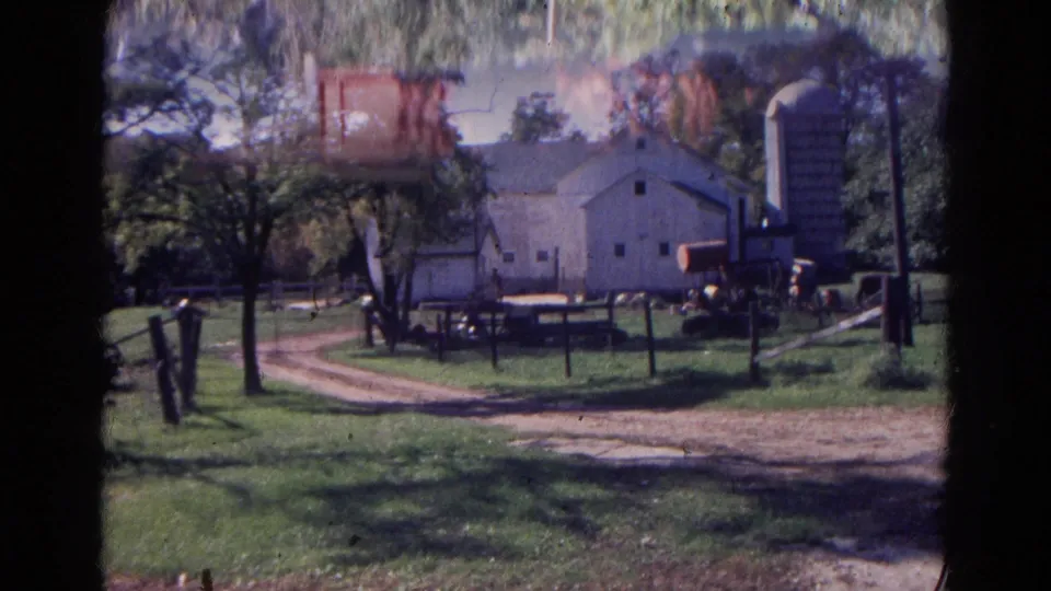 1968 Wauconda farmyard view with a white barn, tall silo, fencing, trees, and a curving dirt drive.