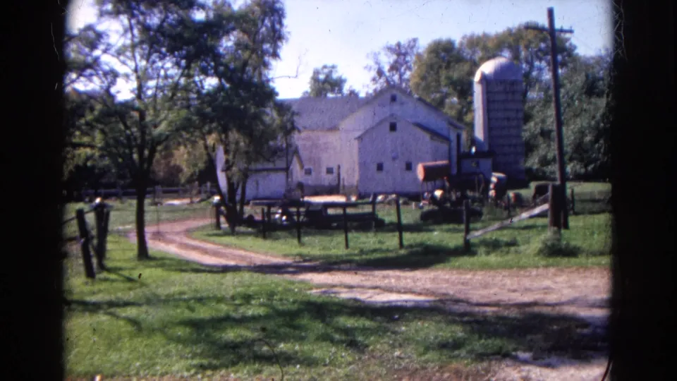 1968 Wauconda, Illinois farmyard with a white barn, tall silo, fencing, trees and a curving dirt drive.