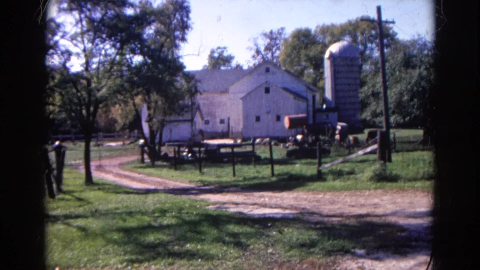 The camera holds on the Wauconda farm scene, showing the barn, silo, fence line, trees and dirt driveway.