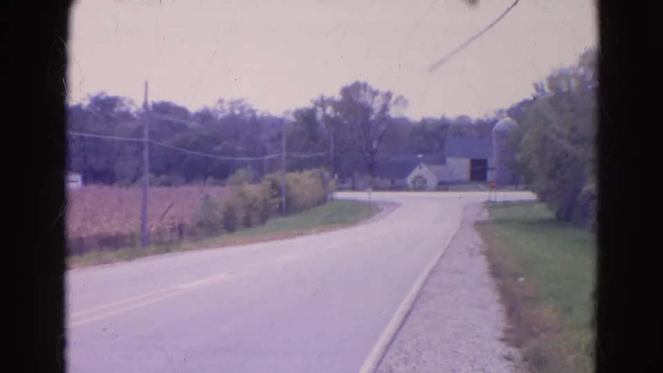 The road curves through rural Wauconda after the truck has passed, leaving cornfield, utility poles, farm buildings, and roadside grass visible.