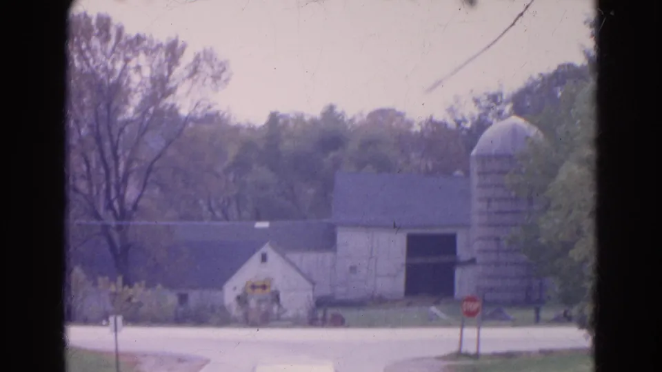 1968 Wauconda farmstead at a rural intersection, with a white building, tall silo, stop sign, road, trees, and film gate edge.