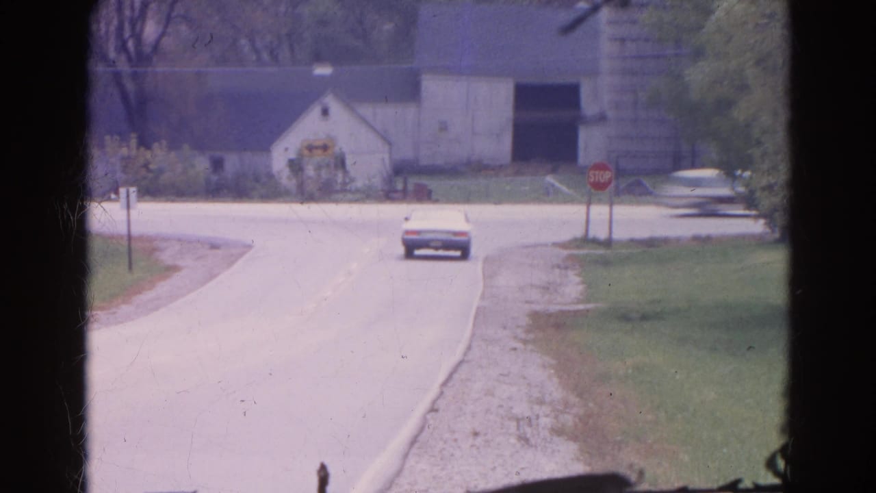 1968 Wauconda, Illinois 8mm frame showing a white sedan near a rural intersection with a stop sign, barn, silo, and grassy roadside.
