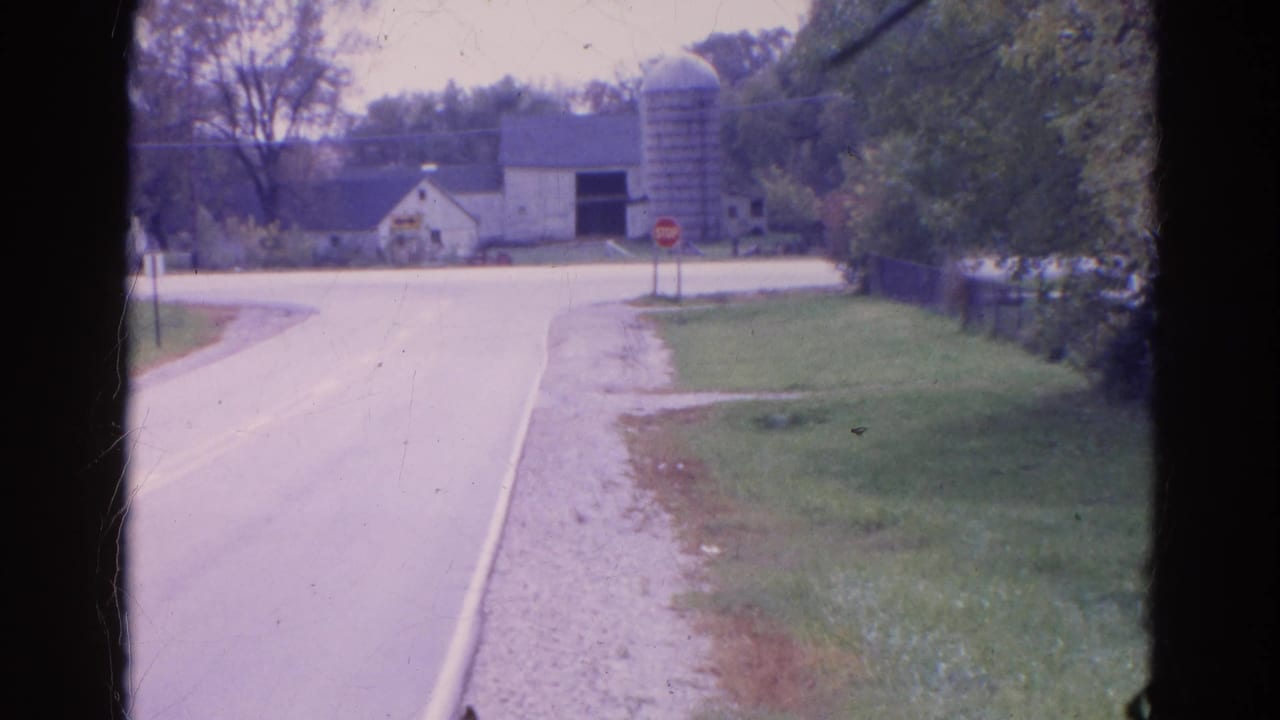 Roadside view of a rural intersection with a stop sign, barn, silo, and trees.