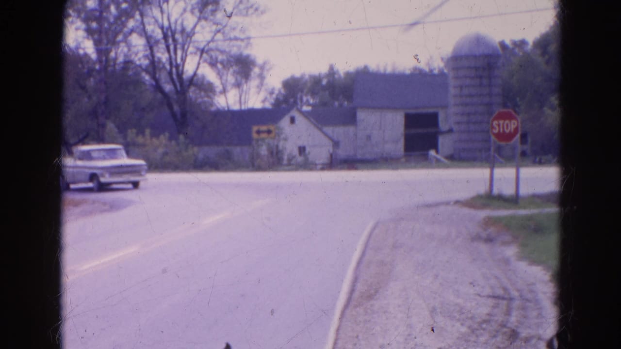 White pickup truck approaches a rural intersection near a barn, silo, and stop sign.