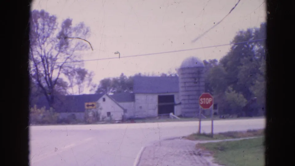 1968 Wauconda, Illinois frame with stop sign at a farm-adjacent intersection, including a barn, silo, trees, and pale sky.