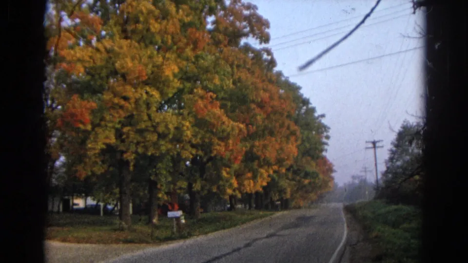 1968 Wauconda frame with fall foliage beside a quiet road, overhead utility wires, roadside poles, and soft 8mm edge shadowing.